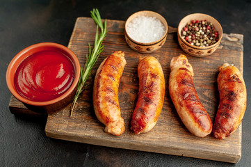 Grilled sausages with spices, ketchup and rosemary on a stone table, ready to eat
