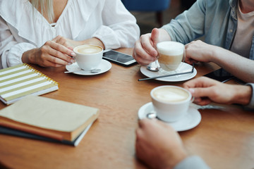 Hands of college friends gathered by table in cafe after classes for a drink