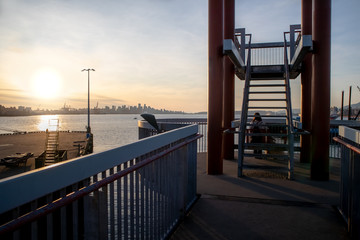 City waterfront view at sunset. A person sitting with a dog on a bench. Lookout tower with view of downtown Vancouver, BC, Canada