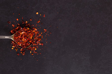 Crushed dried chili peppers in an iron spoon scattered on a black background. Concept, copy space.