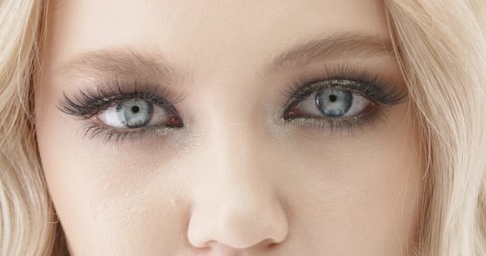 Close up shot of a beautiful caucasian girl wearing bright make up opening her eyes with blue irises and looking at camera 4k footage