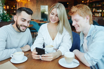 Pretty young smiling woman and two happy guys watching video in smartphone