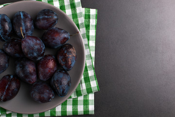Fresh appetizing plums in a gray bowl, summer concept, copy space.