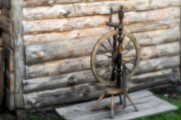 Blur soft light. Ancient spinning wheel in the yard on the background of logs. Background. Concept of vintage needlework