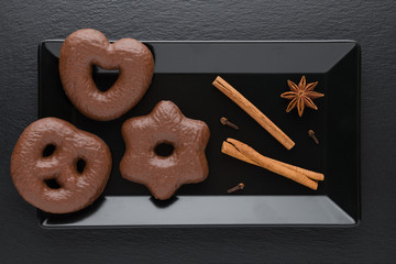 traditional german christmas chocolate gingerbread lebkuchen with cinnamon sticks, anise and clove on black plate