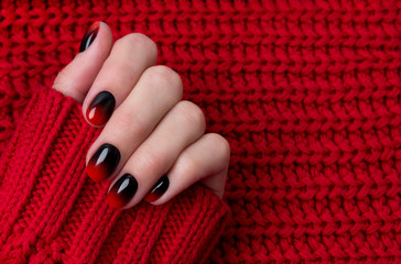 Female hand with red black ombre gradient nails in sweater