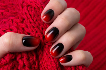 Female hand with red black ombre gradient nails hold wool textile fabric © Darya Lavinskaya