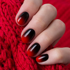 Female hand with red black ombre gradient nails hold wool textile fabric © Darya Lavinskaya