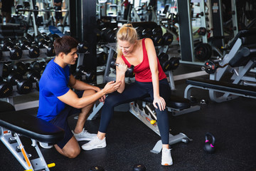 Fototapeta na wymiar Caucasian Woman lifting dumbbell and exercise in the gym with Trainer or instructor Asian man teaching. spoty girl using hand for weight training while personal trainer supervises her progress