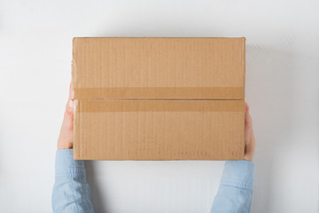 Large square cardboard box in female hands. Top view, white background