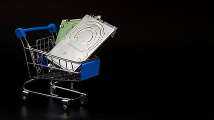 Two laptop hard drives in a blue shopping basket. Black background. Sale and discount concept, black friday, cyber monday, computer peripherals and accessories. Copy space. Template for design banner.