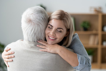 Happy young affectionate woman with toothy smile giving hug to her senior father