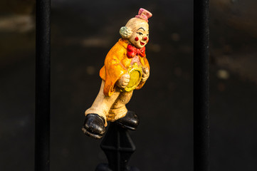Fröhliche Clownsfigur in Seitenansicht als Spielzeug mit einem Lächeln im Gesicht auf einen Zaun aufgesteckt und hintern Gitter aus Metallstäben