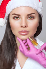 Cosmetologist does prp therapy on the face of a beautiful woman in a Santa Claus hat.New Year's and...