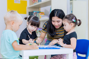 Asian teacher helps her students to paint on paper