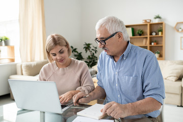 Pretty young woman with laptop and her retired senior father searching for data