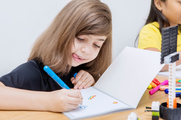 Caucasian little girl drawing with crayon in the class