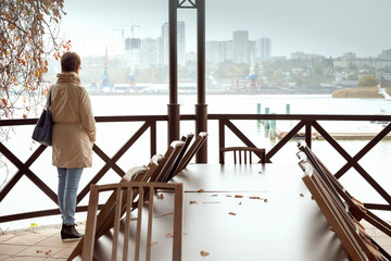 Naklejka premium lonely woman stands in an abandoned restaurant on the river Bank and looks at the city in the distance. Psychology, the problem of loneliness.
