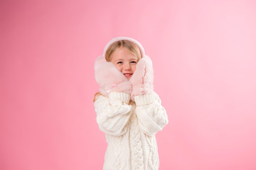 little girl the blonde smiles pink mittens and headphones on a pink background, the concept of winter clothing