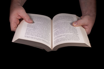 Naklejka premium Ein aufgeschlagenes Buch von zwei Händen gehalten vor schwarzem Hintergrund