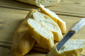 Sliced french baguette. Freshly baked traditional french bread on a wooden table next to a kitchen knife.