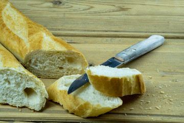 Freshly baked traditional french bread on a wooden table next to a kitchen knife. Sliced french baguette.