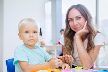 Little boy and teacher gluing trinkets in kindergarten