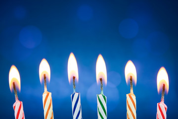 Colorful and funny birthday candles are lit on a blue background. Birthday party, anniversary or some celebration where the candles are ready for someone to blow them. Background with beautiful bokeh