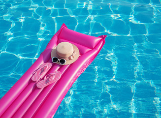 Beach summer holiday background. Inflatable air mattress, flip flops and hat on swimming pool.