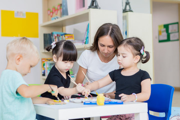 Fototapeta premium Nursery teacher with her students painting draws