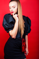 Fototapeta premium young pretty lady in black suit and small handbag posing on red background, lifestyle people concept