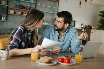 Fototapeta na wymiar Young couple arguing while having problems with their home finances at dining table