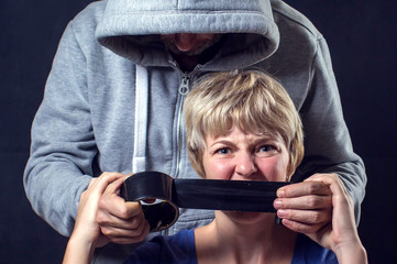 Man's hand covering a woman'smouth with scotch tape. Concept of violence or kidnapping.