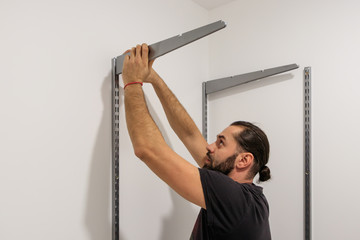 A working fitter man with a beard mounts metal racks on the wall.