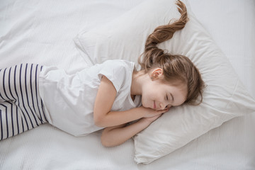 Cute little girl with long hair sleeping in bed.