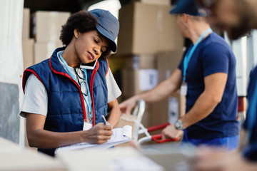 African American worker taking notes while talking on mobile phone during a delivery.