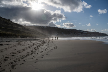 Sea spray being blown off the sea and onto the shore with sun and silhouettes