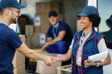 Two happy delivery workers shaking hands outdoors.