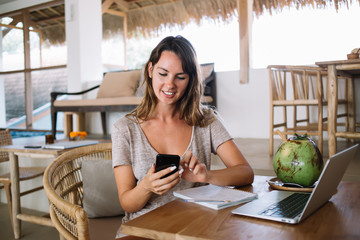 Happy female blogger enjoying read received cute messages from web followers during digital nomad...