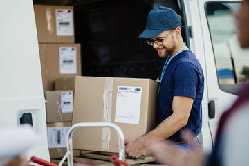 Young manual worker unloading cardboard boxes from a delivery van.
