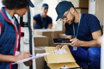 Two workers preparing packages for delivery and scanning bar codes with digital tablet.