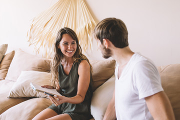 Obraz premium Cheerful man and woman discussing funny information or publication from social network during leisure day in home interior, positive hipster guys enjoying fellow relationship in cozy apartment