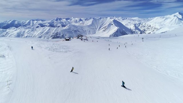 Skiers and snowboarders riding down the mountain slope. Aerial flight above mountain ski resort Gudauri, Georgia