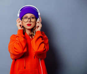 Style girl in orange hoodie and purple hat with headphones on grey background