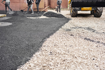 Laying new asphalt, covering the pit, on the rubble. Workers carry in shovels and using asphalt lute for smooth, hot asphalt.