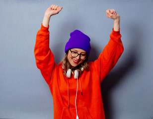 Style girl in orange hoodie and purple hat with headphones on grey background