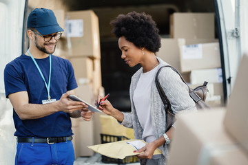 Black woman signing on digital tablet after receiving package from a courier.