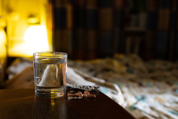 some of medicine pills and a glass of water  on a nightstand next to the bed at night, treatment insomnia concept