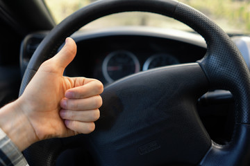 first person view of driver showing thumb up in front of steering wheel