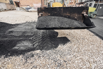 A tractor unloads the asphalt. Large heavy machinery is carrying out road repair work. Laying new asphalt. Construction of a new asphalt road.